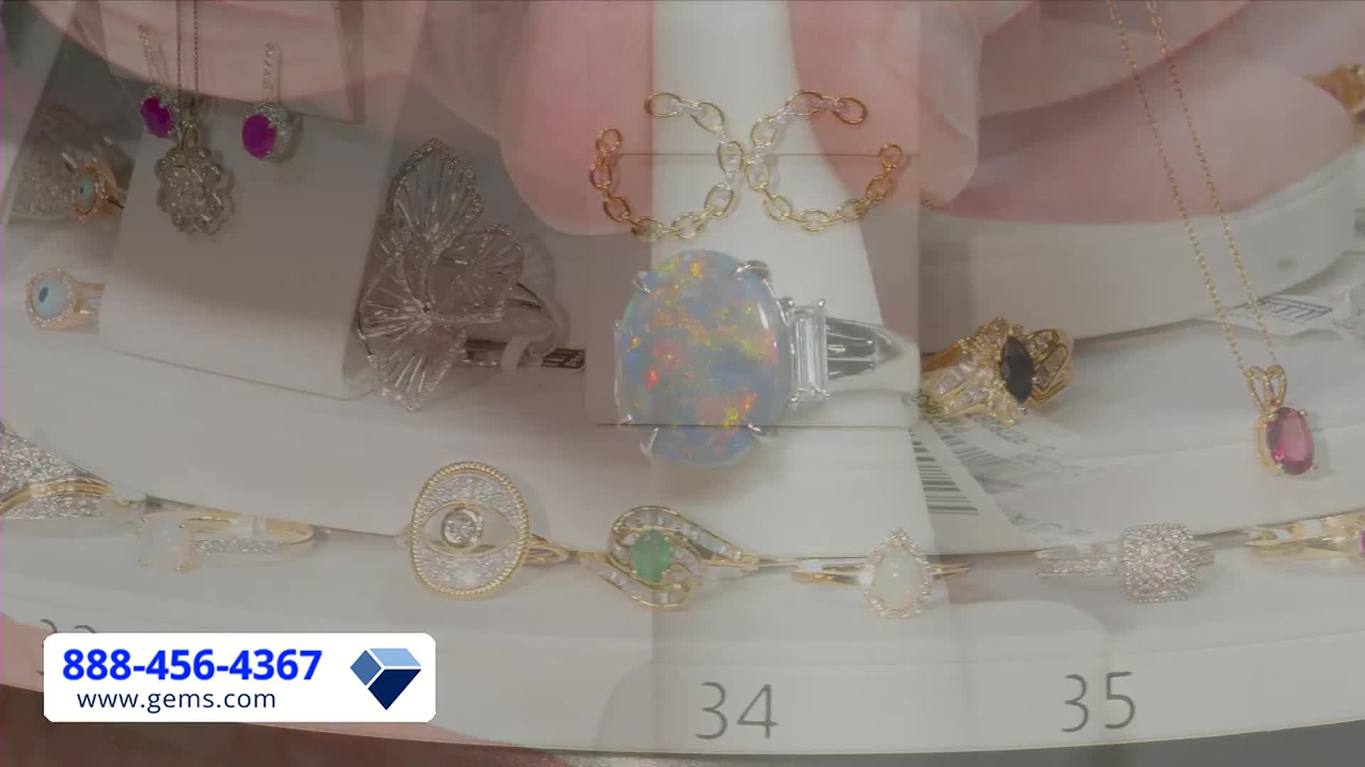 A hand displays a large opal ring, framed by a collection of other jewelry. The Gem Shopping Network's phone number and website are visible in the corner.
