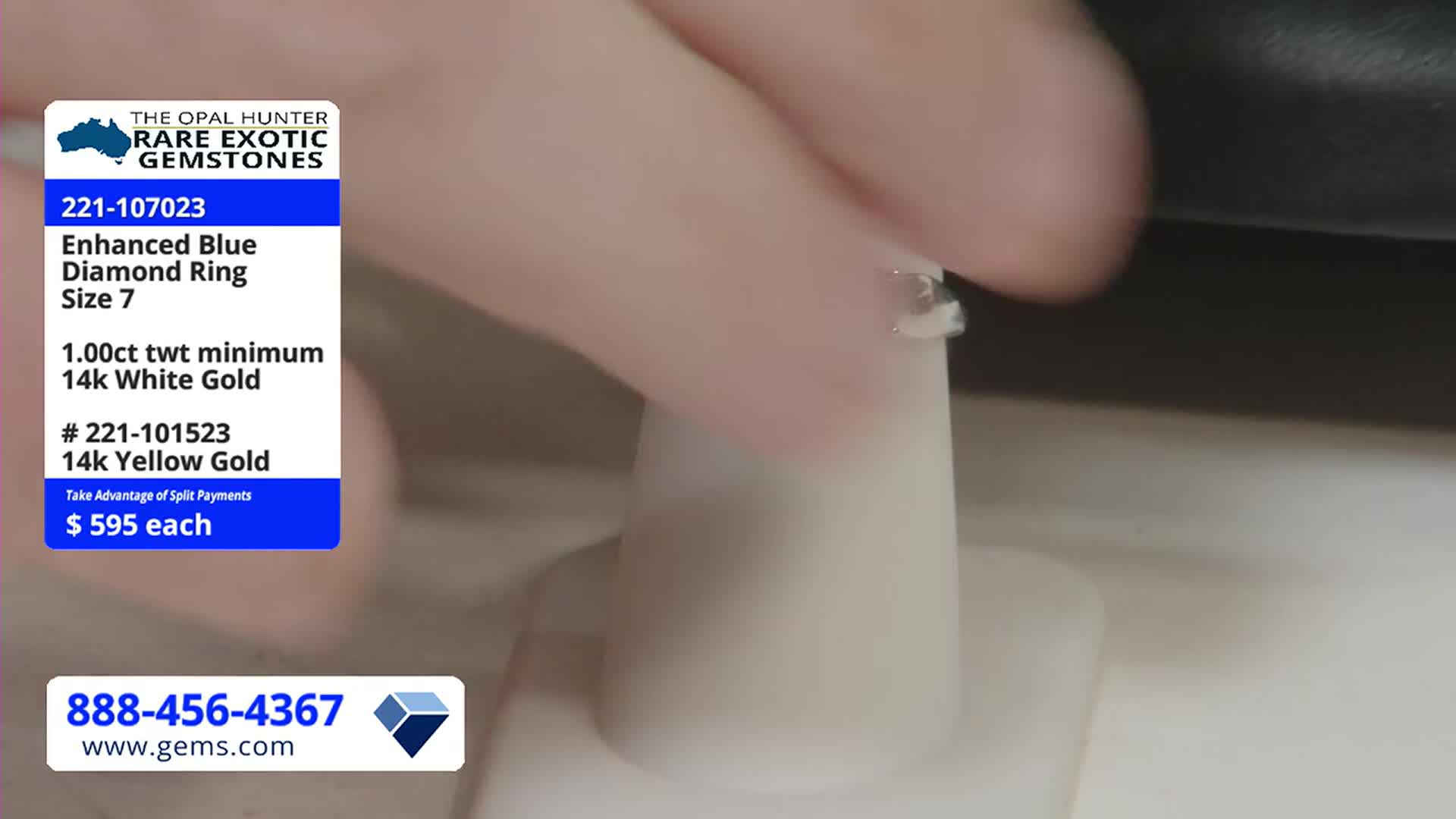A hand carefully places a ring on a small, white display stand. The Gem Shopping Network logo and product details are visible in the corner.

