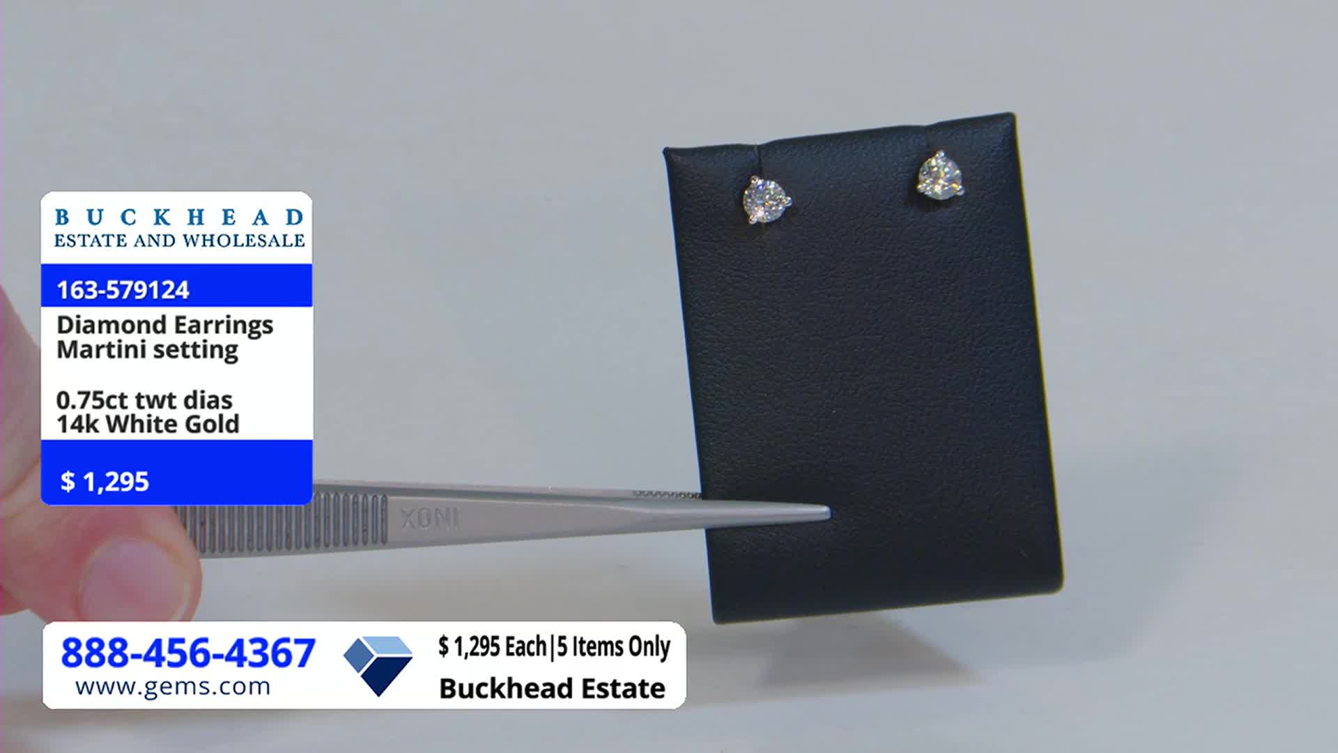 A pair of diamond earrings sits on a black display, each stone sparkling under the lights. The host is holding a pair of tweezers, ready to show off the jewelry on the Gem Shopping Network.
