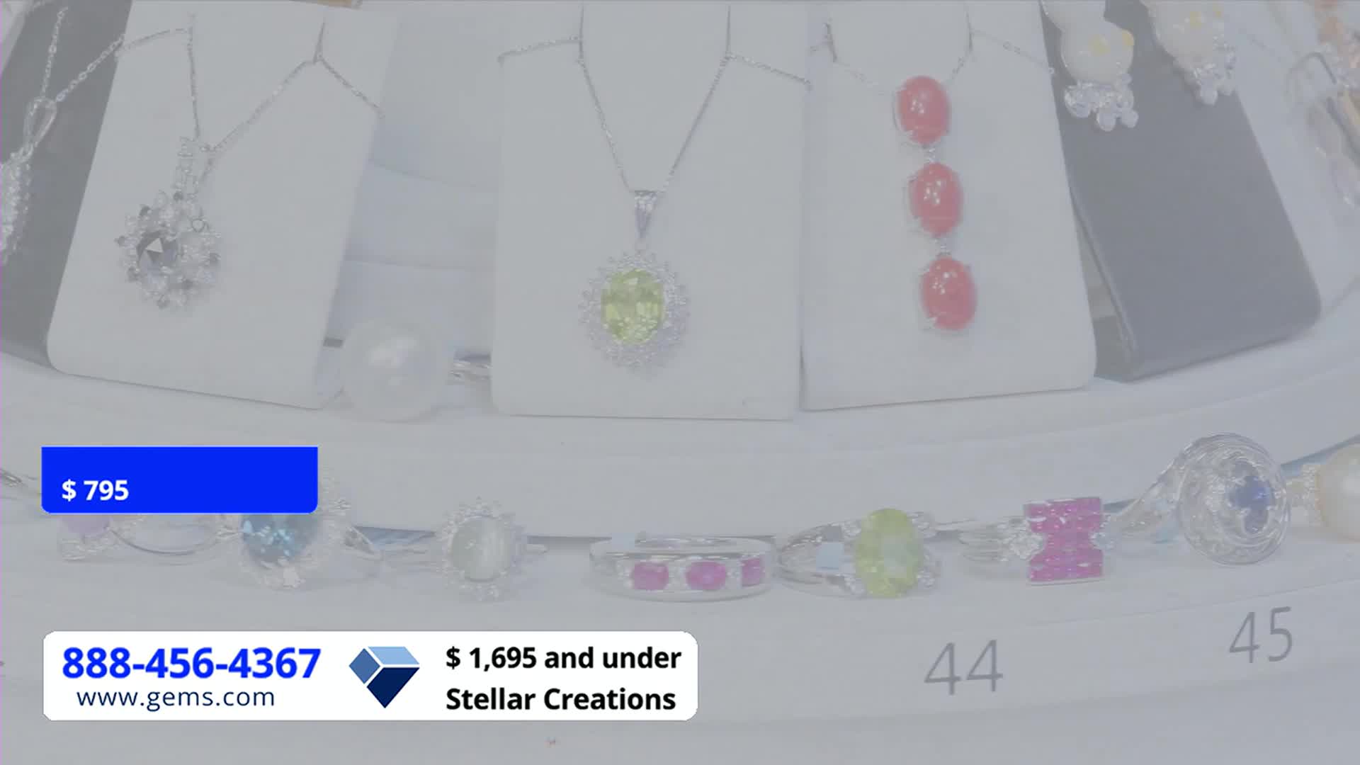 Jewelry, displayed on white stands, is lit by bright lights. A blue banner with a price tag sits in the corner, and a phone number for Gem Shopping Network appears below.
