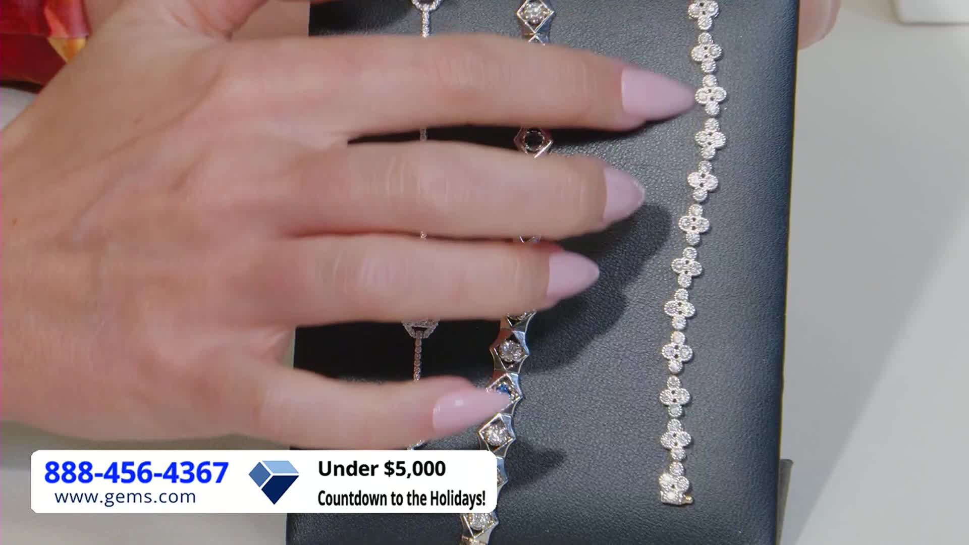 A hand with polished nails gently sweeps across a selection of diamond bracelets, showcasing their sparkle. The Gem Shopping Network logo and a phone number are visible at the bottom of the screen.
