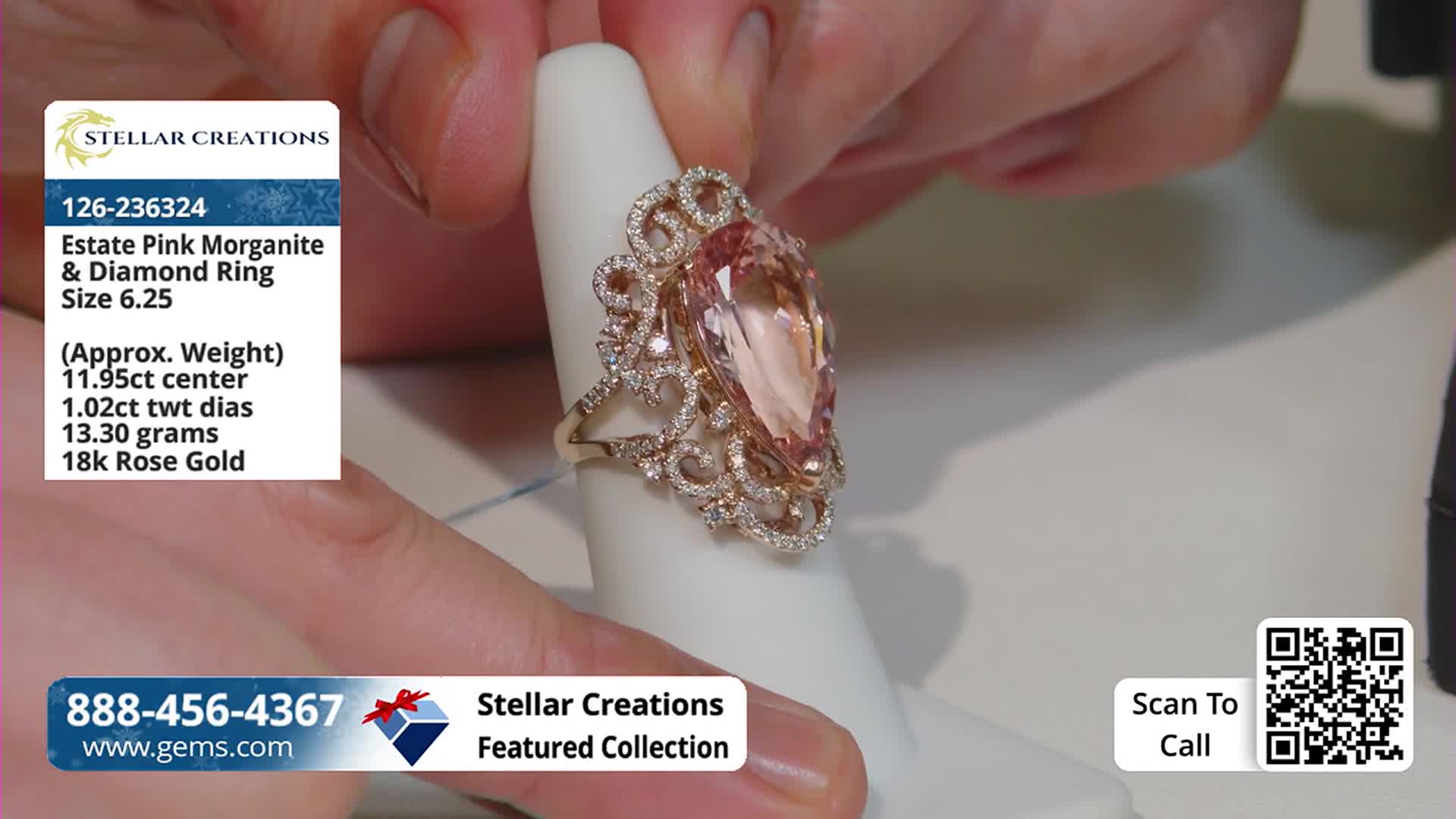 A hand gently holds a ring with a large, peach-colored stone on a white display stand. The ring is ornate, with smaller diamonds surrounding the main gem.
