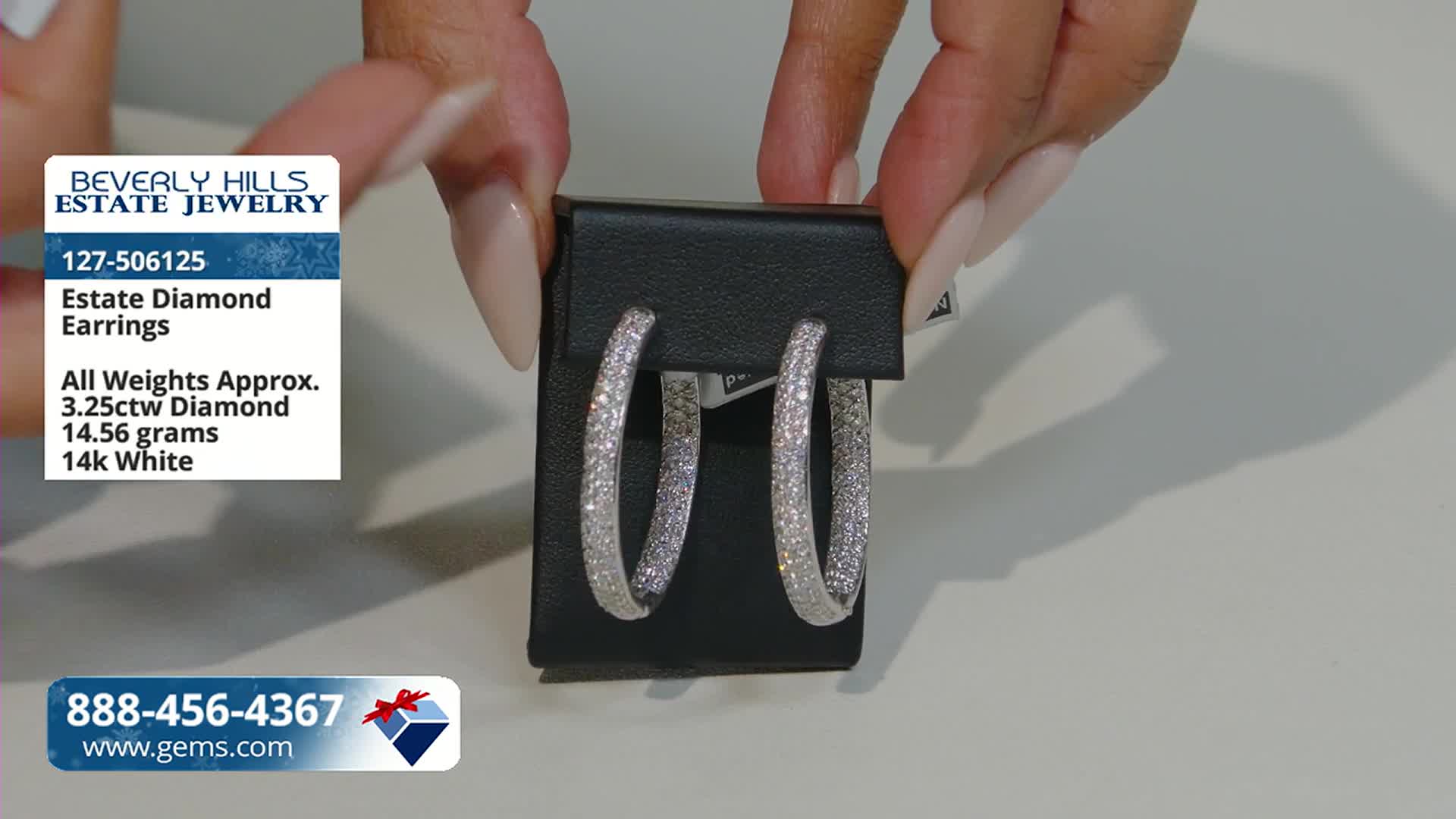 A pair of diamond-studded hoop earrings is held up for display. The Gem Shopping Network graphic in the corner provides details about the jewelry.
