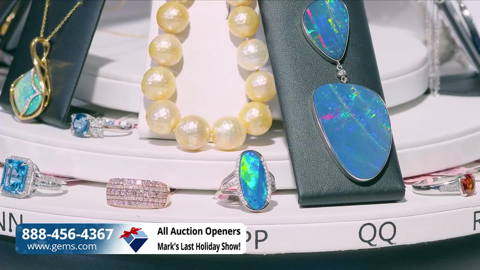 A rotating display showcases various jewelry pieces, including rings and a pearl necklace, all brightly lit. The Gem Shopping Network logo and a phone number are visible at the bottom of the screen.
