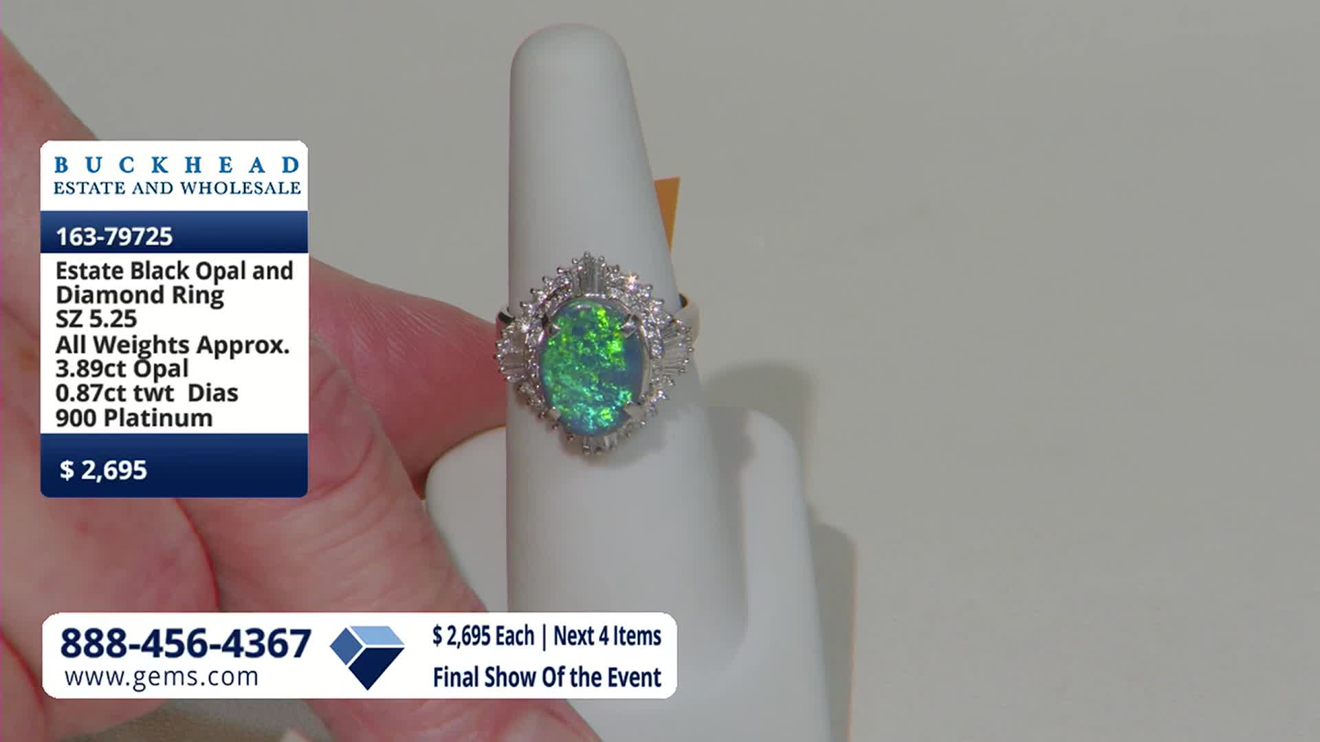 A hand holds a ring featuring a dark opal with vibrant green and blue flashes, surrounded by small diamonds. The Gem Shopping Network logo and pricing information are displayed on a blue card to the left.