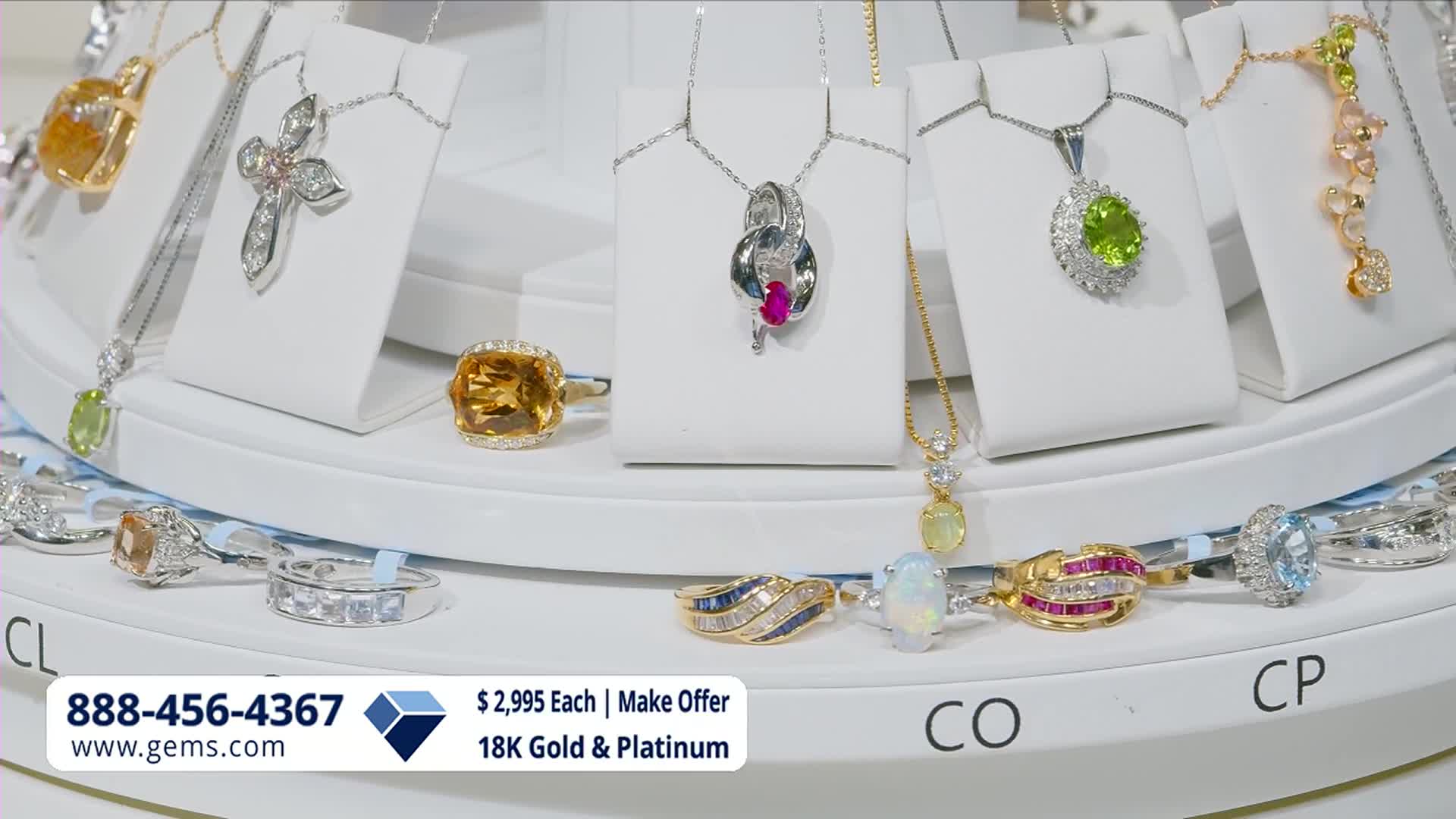 A display of necklaces and rings sits on a rotating platform, showcasing sparkling gemstones. The Gem Shopping Network's contact information is visible at the bottom.