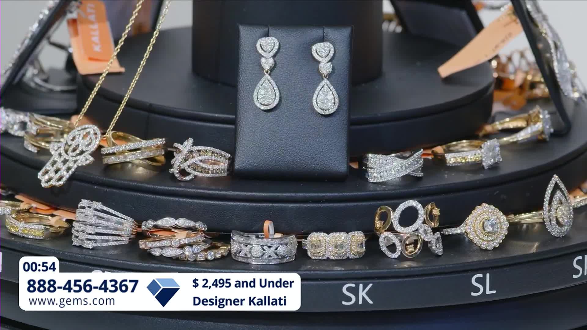 A display of diamond rings and earrings rotates on a stand. The Gem Shopping Network logo is visible at the bottom of the screen.