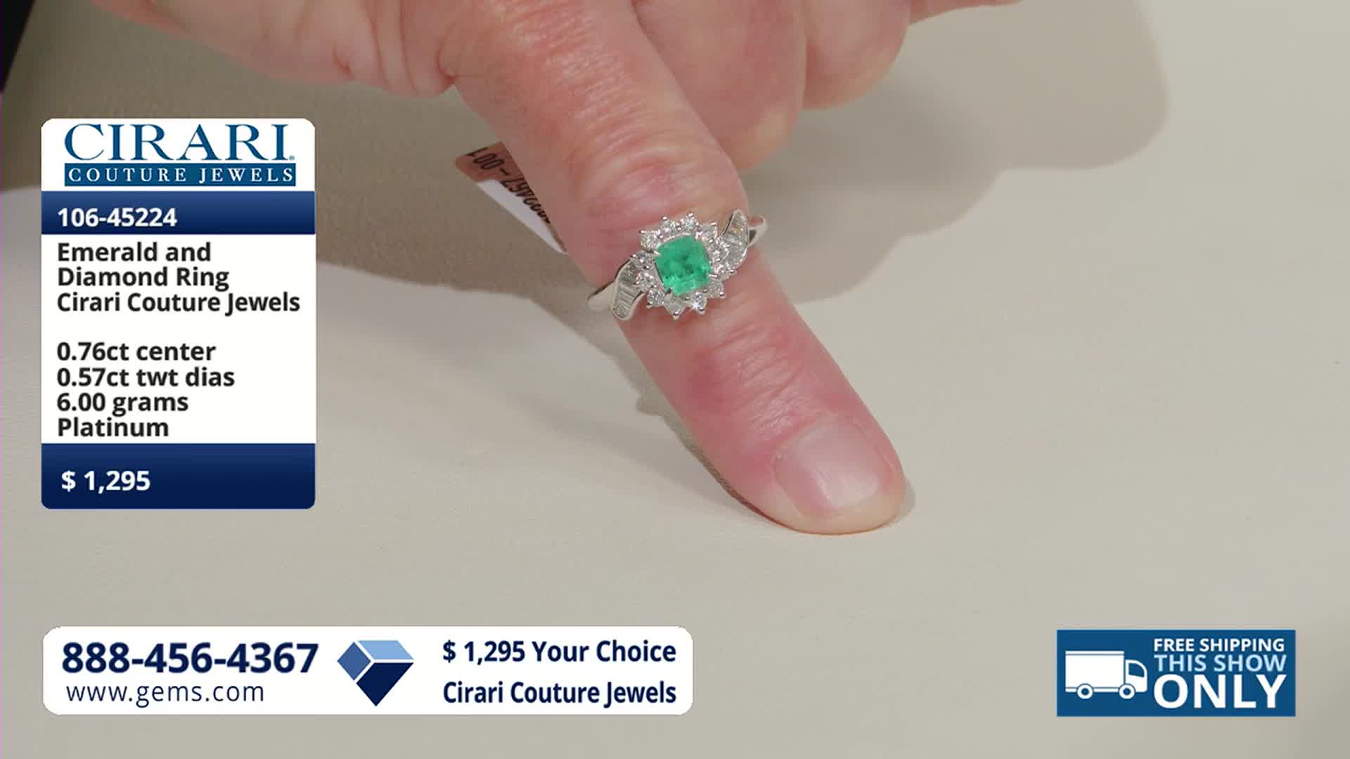 A hand displays a platinum ring with a central emerald surrounded by diamonds. The ring is priced at $1,295 and is available from Cirari Couture Jewels.