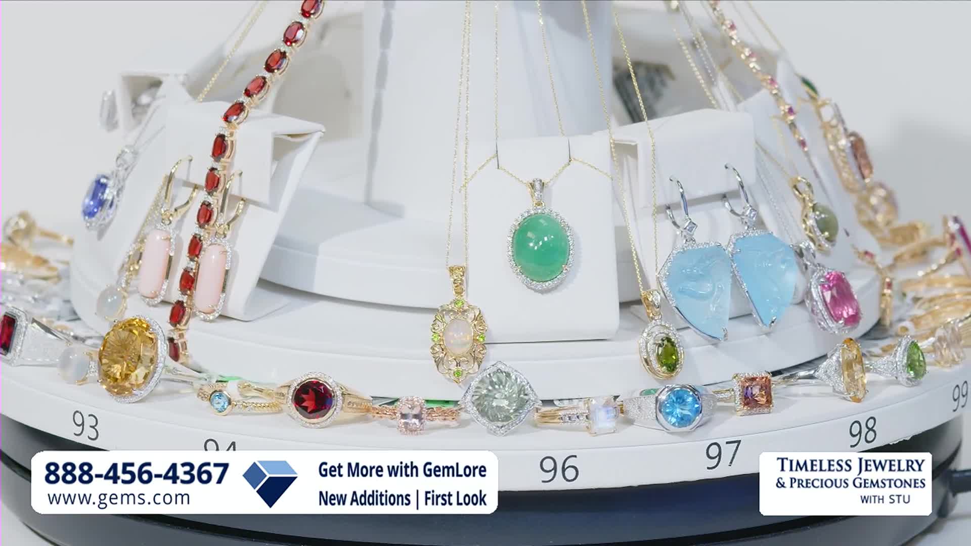 The display spins, showcasing a variety of necklaces and rings. A large oval green jade pendant hangs prominently, catching the light.