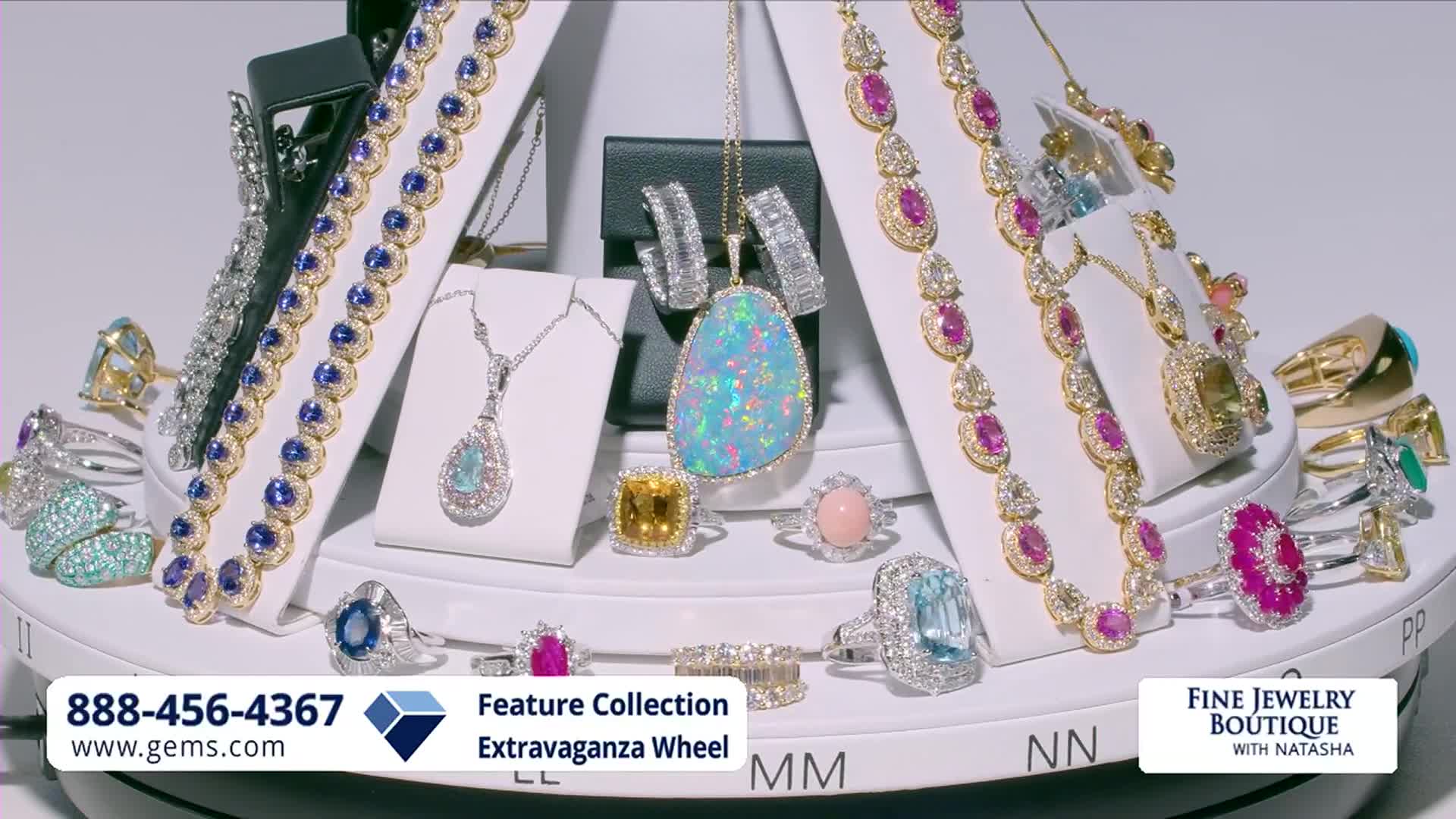 The display of fine jewelry is slowly rotating. A large opal pendant hangs from a gold chain, surrounded by diamond earrings.