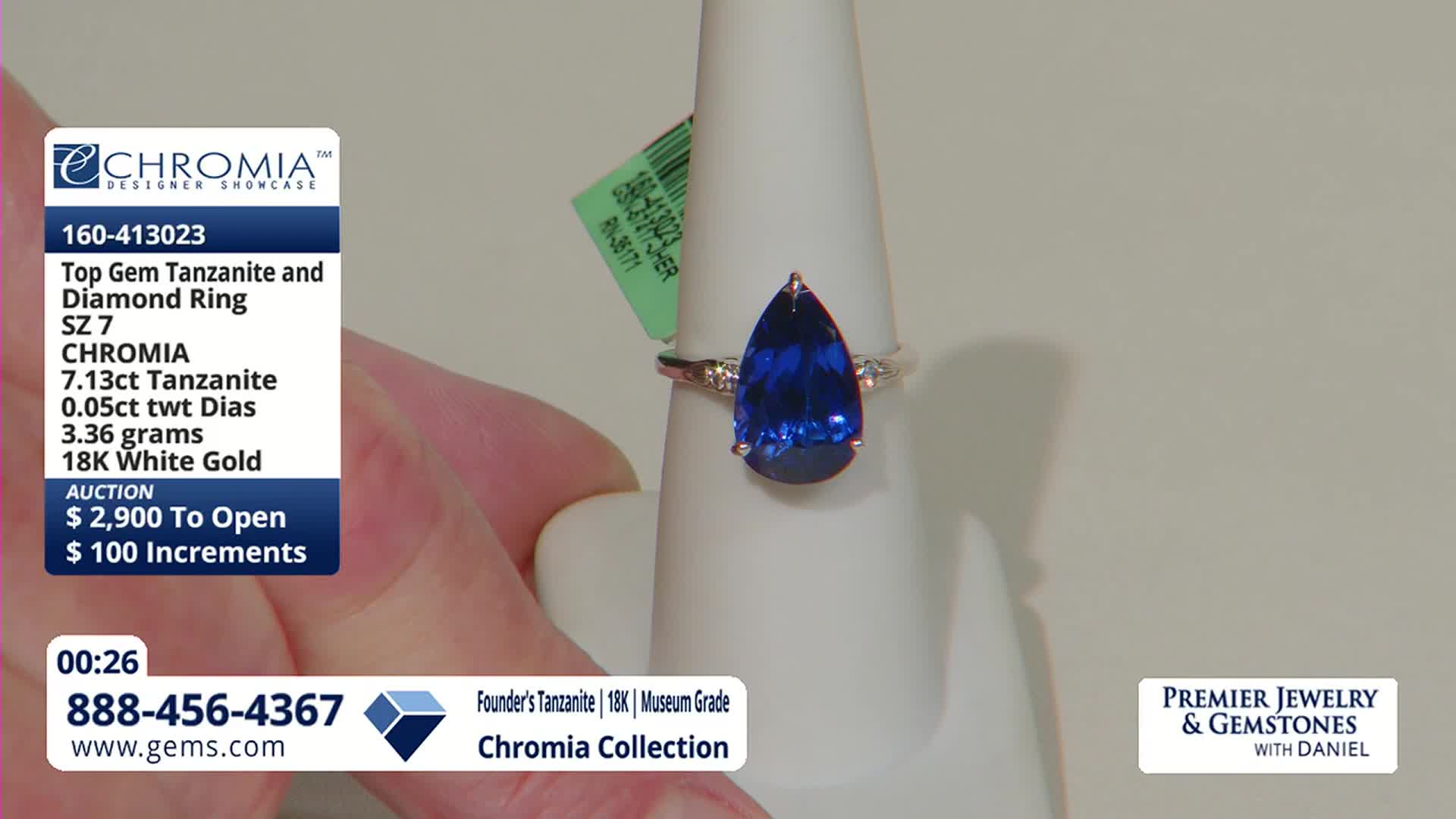 A large, pear-shaped tanzanite ring with small diamonds sits on a white display. The Gem Shopping Network is broadcasting this designer showcase from the United States.