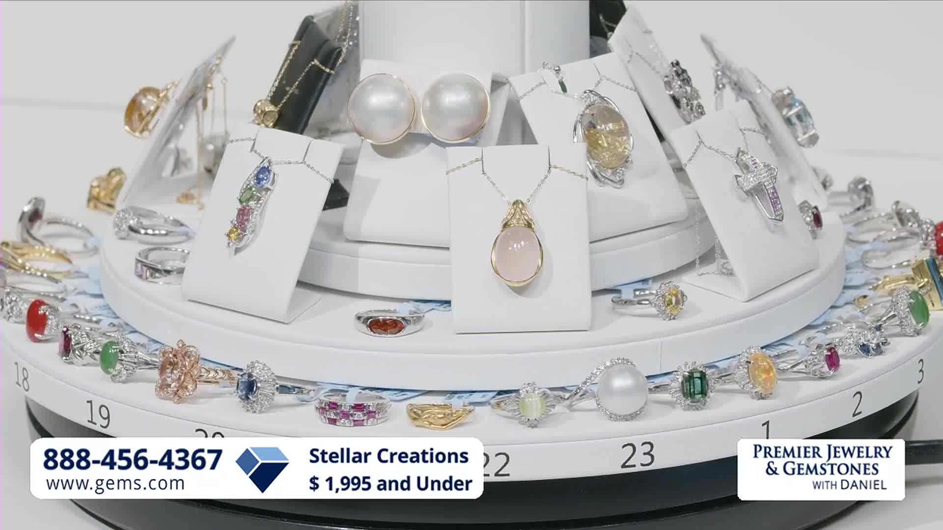 A display of fine jewelry, featuring rings and necklaces with colorful gemstones, slowly rotates. The Gem Shopping Network logo and a phone number are visible at the bottom.