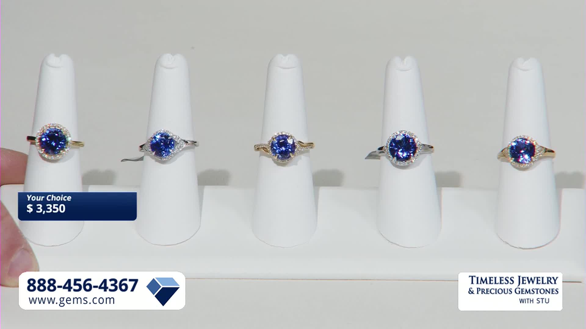 A hand reaches out, pointing to a display of five rings, each featuring a vibrant blue gemstone. The Gem Shopping Network logo and a price of $3,350 are visible on screen.