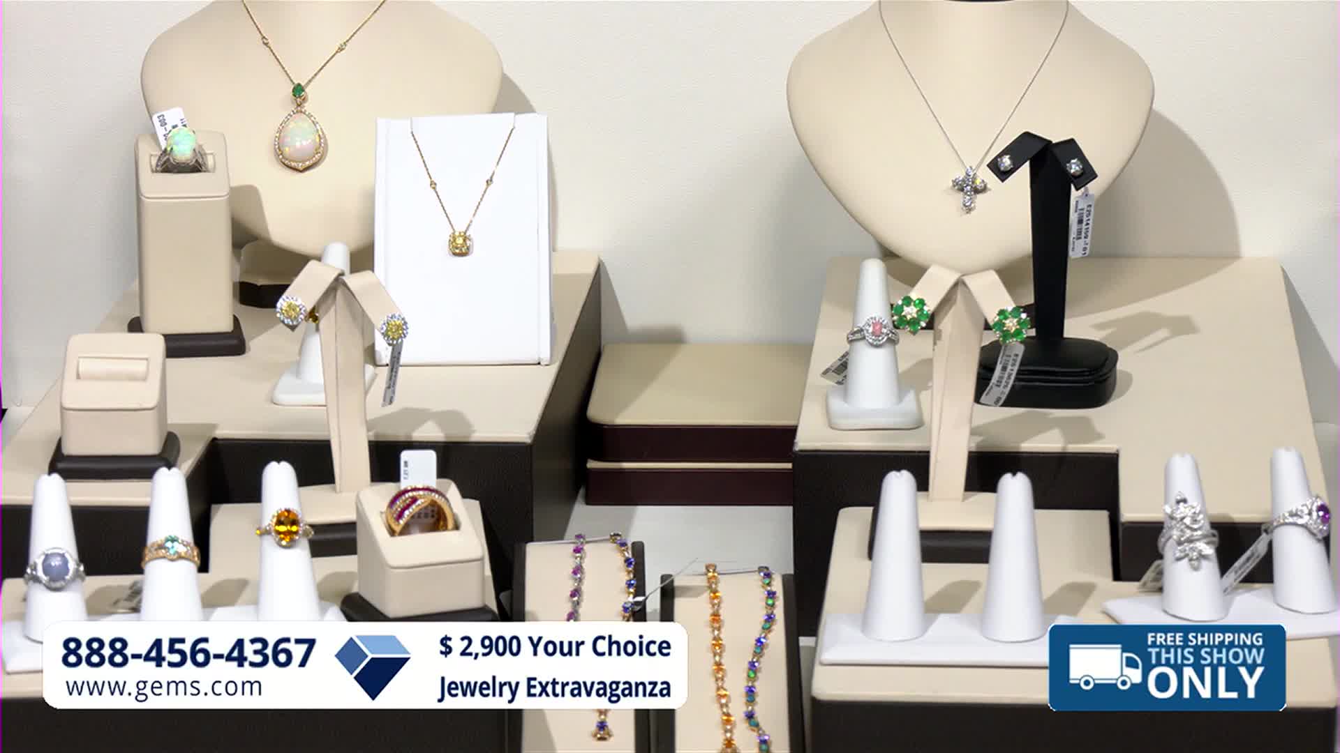 A display of fine jewelry sits on tiered stands, showcasing necklaces, earrings, and rings. The Gem Shopping Network logo and a phone number are visible at the bottom of the screen.