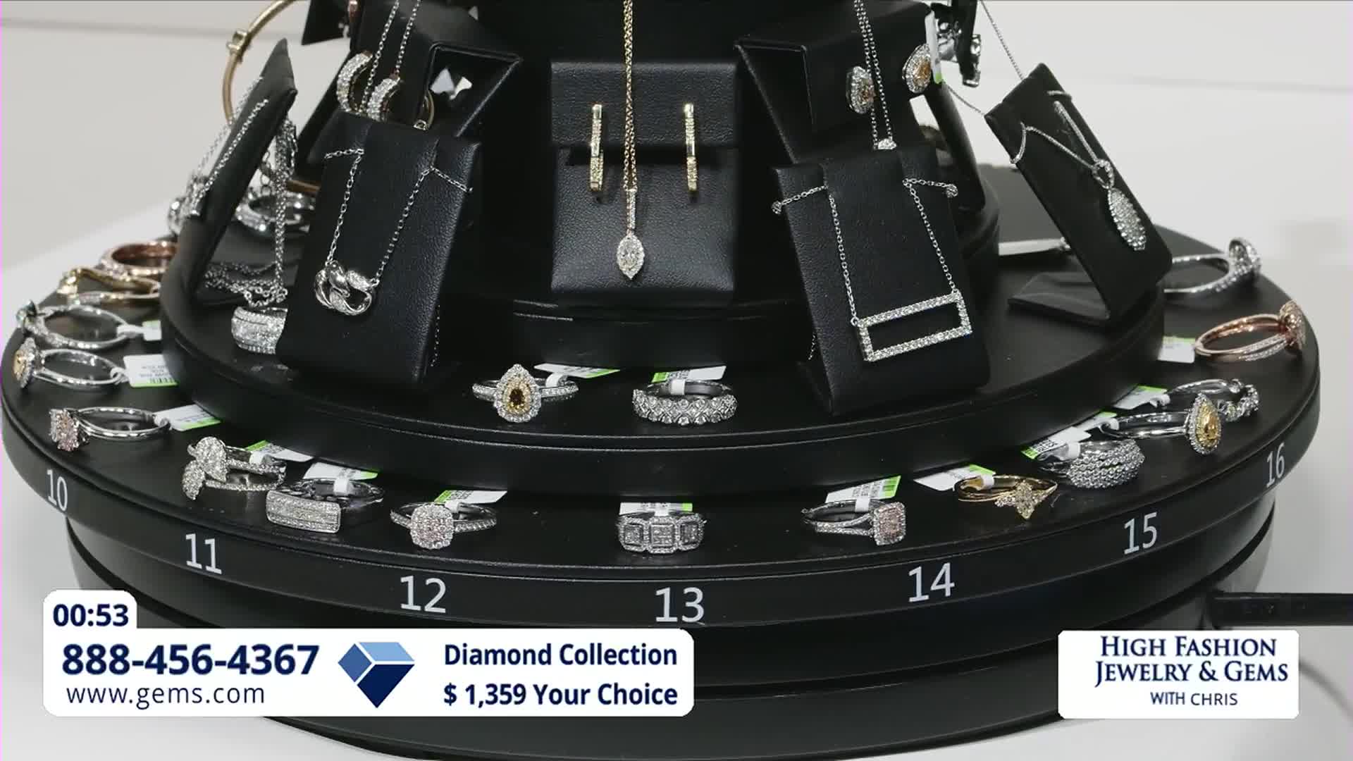 The jewelry display slowly turns, revealing rings and necklaces. A diamond ring with a pear-shaped stone catches the light.