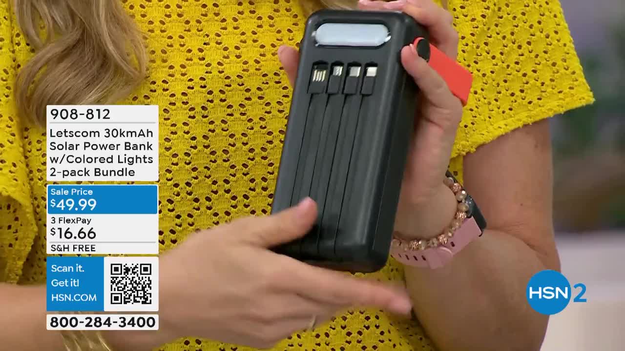 A woman in a yellow top holds a black power bank with four charging cords extending from it. The HSN2 logo is visible in the corner, and a graphic displays the product's price and features.

