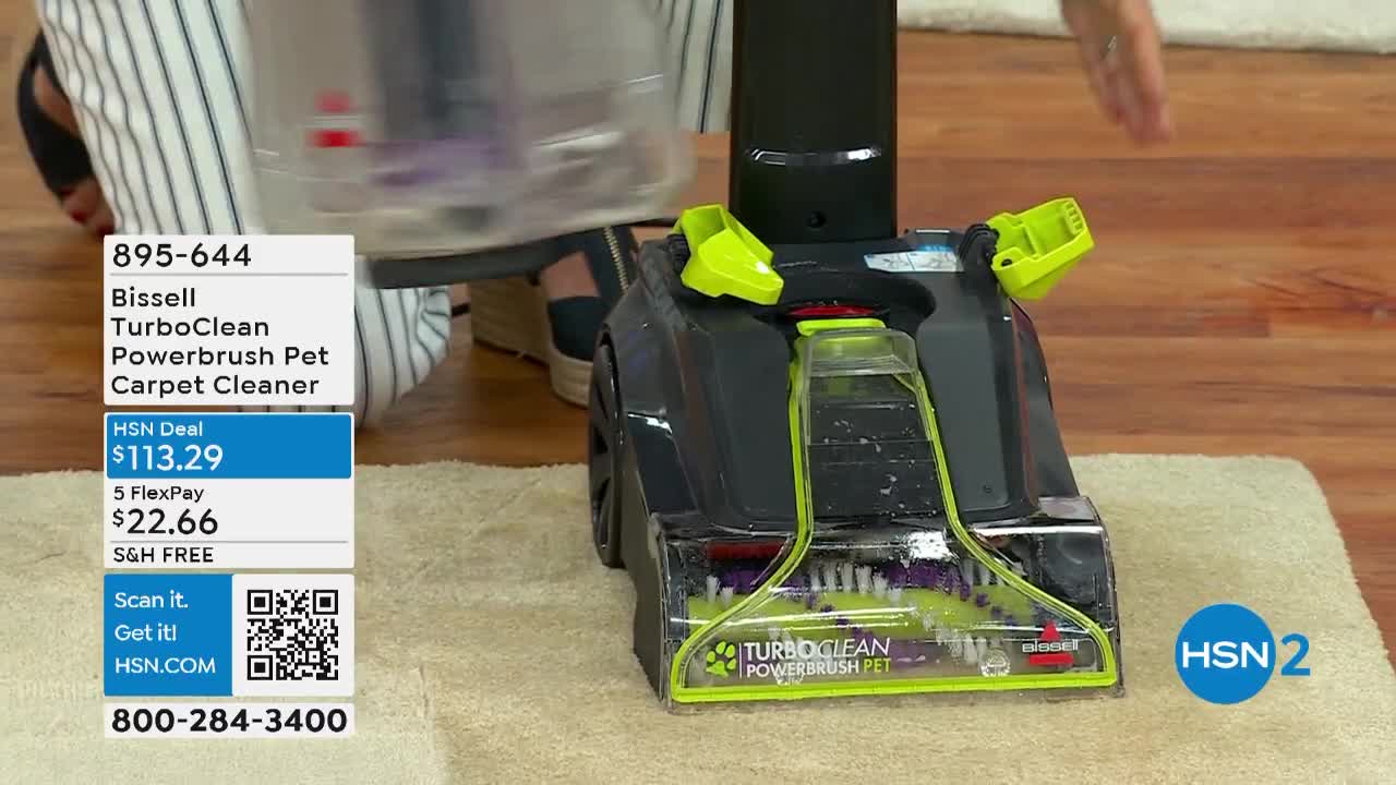 A carpet cleaner, labeled "Bissell TurboClean Powerbrush Pet," sits on a light-colored rug. The HSN2 deal is displayed on a graphic panel, and a person's hand is visible above the machine.
