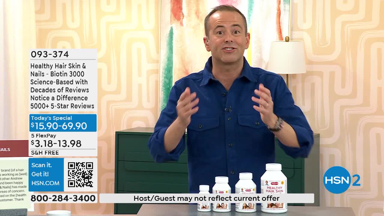 A man in a blue shirt gestures with both hands, talking to someone off-camera. In front of him, several white bottles of "Healthy Hair Skin & Nails" are lined up on a table.
