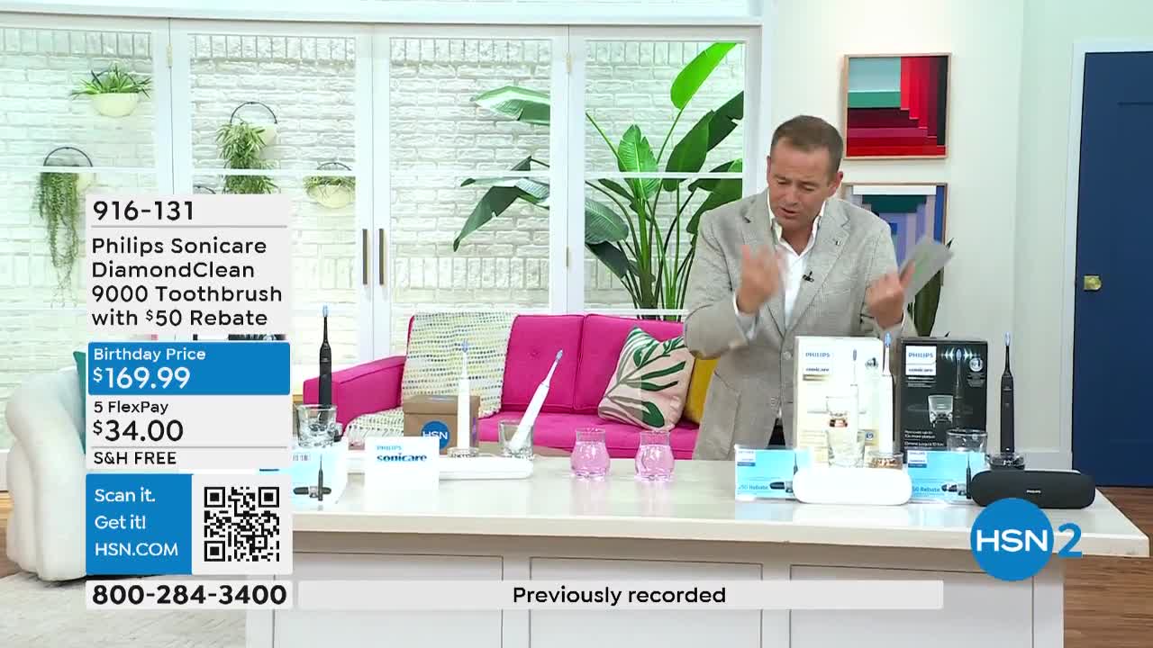 A man in a blazer gestures enthusiastically toward various Philips Sonicare toothbrush boxes and accessories laid out on a white table. The HSN2 logo is visible in the corner, and a graphic on the left displays the item's price.
