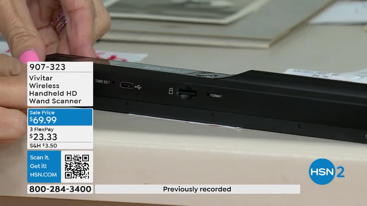 A woman's hand, with pink nail polish, holds a black wand scanner, likely on a set for HSN2. The screen displays the price and features of the Vivitar scanner.
