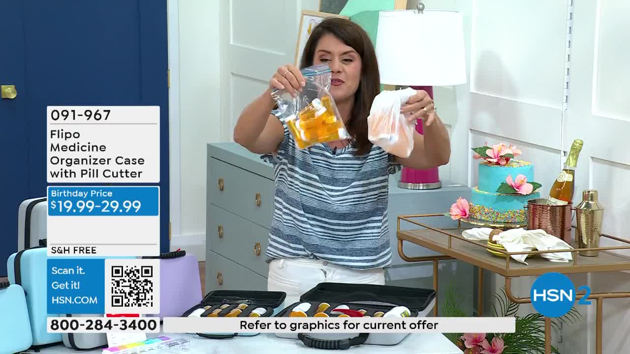 A woman on HSN2 holds up a bag of yellow pills in one hand and a small white cloth in the other. The camera focuses on a medicine organizer case with a pill cutter, displayed on a table.
