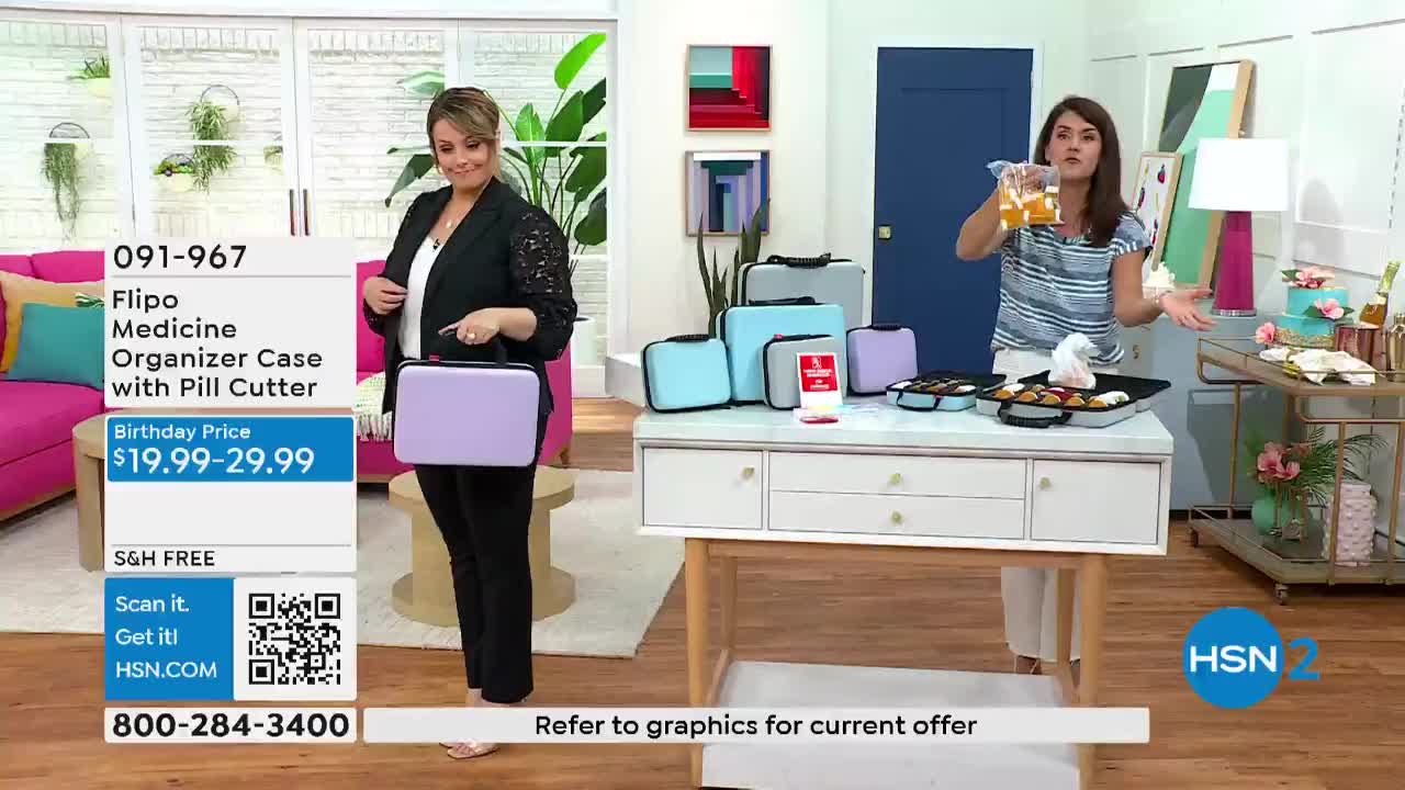 A woman in a black blazer holds a small, lavender case, while another gestures with a bag of liquid. Several medicine organizer cases sit on a white table, along with some treats.
