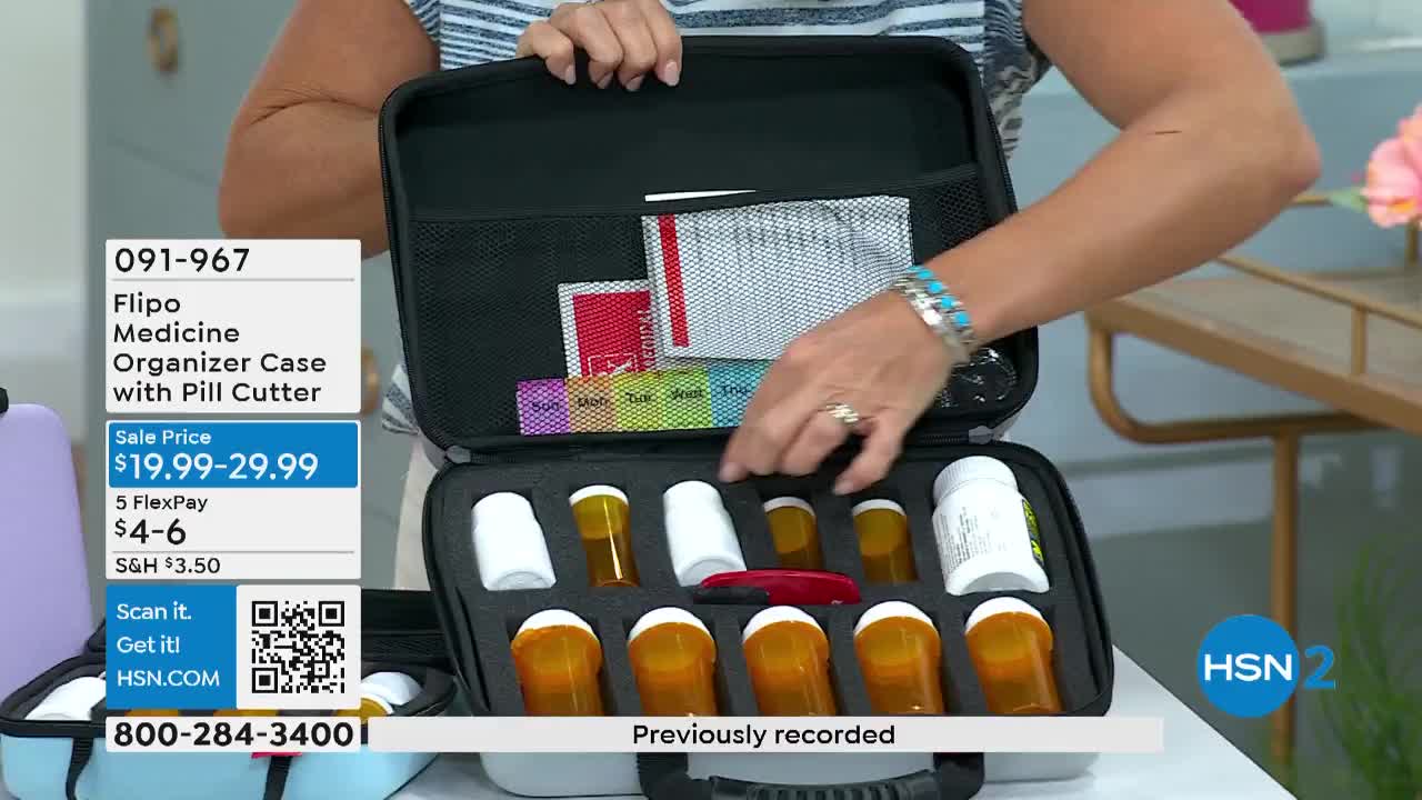 A woman is holding open a black case filled with pill bottles and a pill cutter. She's pointing at a weekly pill organizer in the case's top compartment.
