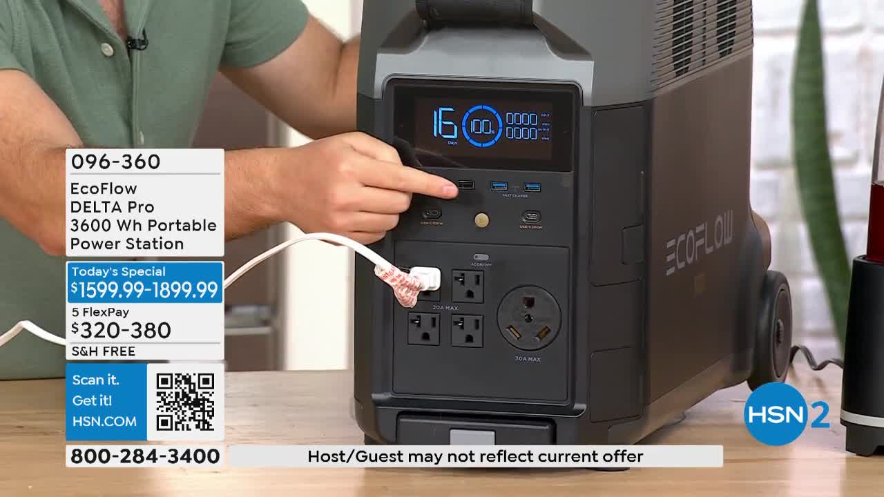 A hand presses a button on a black power station, its digital display showing a blue readout. A white cable with a connector is plugged into the unit, as seen on HSN2.
