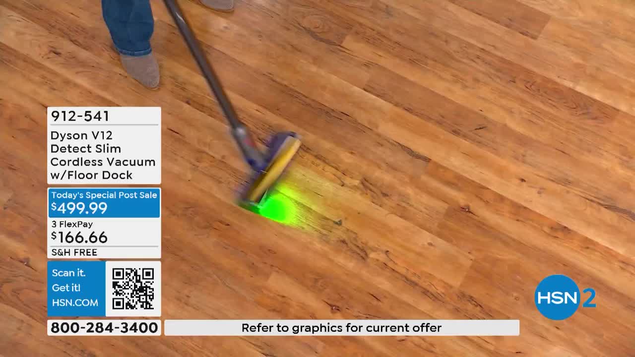 A vacuum cleaner head, lit with a green glow, glides across the wood floor on HSN2. The product is being demonstrated, with the price and model number prominently displayed.
