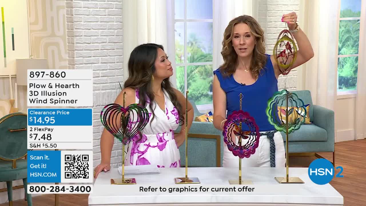 Two women stand behind a table displaying colorful metal wind spinners, one of them holding an oval-shaped one up for the camera. The HSN2 logo is visible in the corner, and a graphic on the left lists the product's price.
