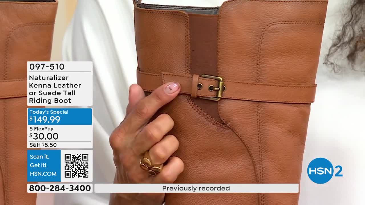 A hand adjusts the strap of a tall brown leather boot. The presenter is showing the details of the boot on HSN2.
