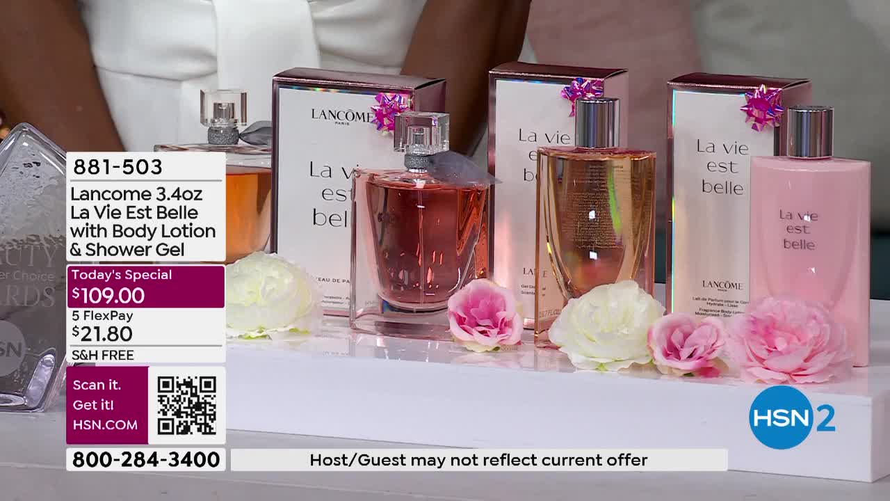 Several bottles of perfume and body lotion sit on a white surface, surrounded by flowers. The HSN2 logo is visible, and a graphic displays the product name and price.
