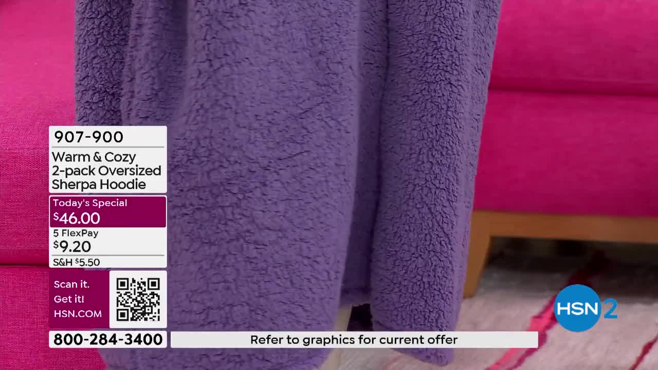 A close-up of a fluffy purple sherpa hoodie fills the screen, with a price tag and the HSN2 logo visible in the corner. The soft fabric is draped over something, and a bright pink couch is in the background.
