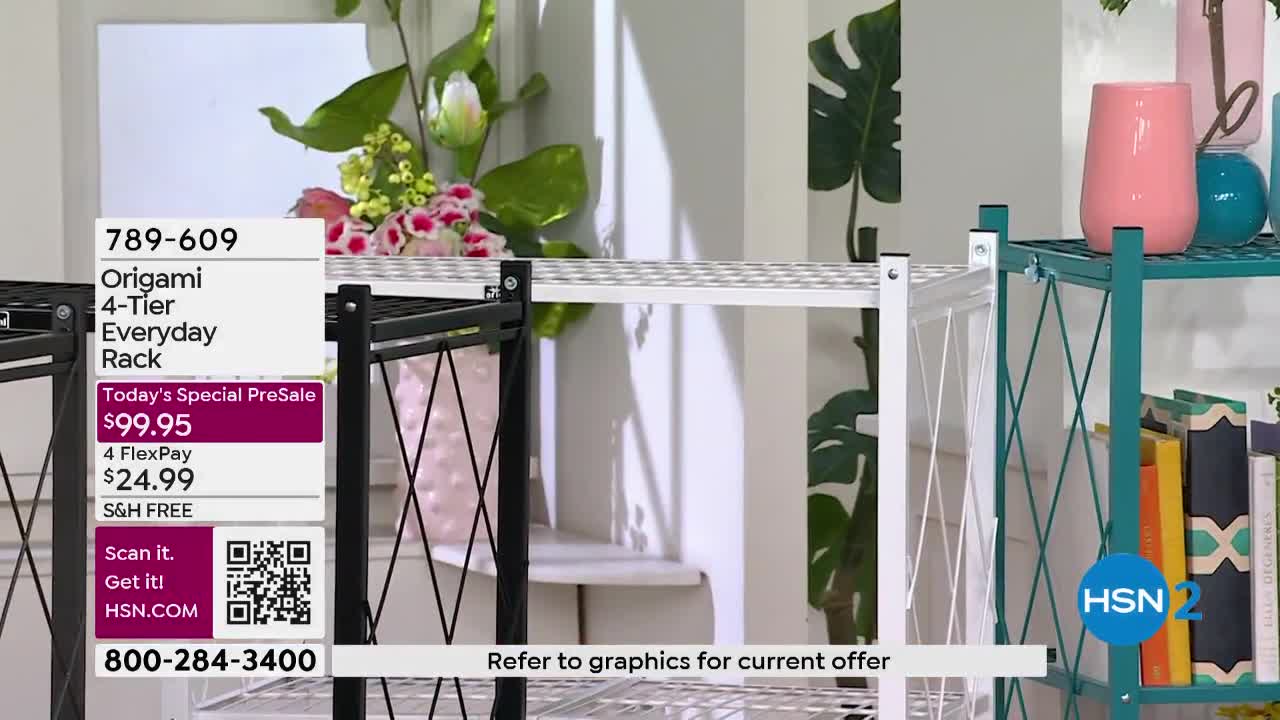A black Origami rack stands next to a white one, both displaying their metal mesh shelves. To the right, a teal rack holds decorative vases and books.