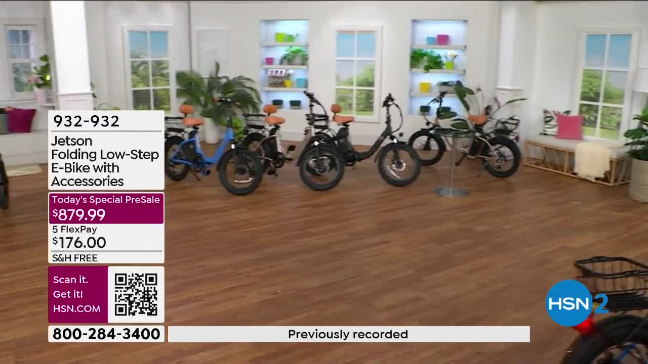 Several Jetson folding e-bikes are lined up on a polished wooden floor. A blue one sits to the left, followed by two black models, and then a green one.