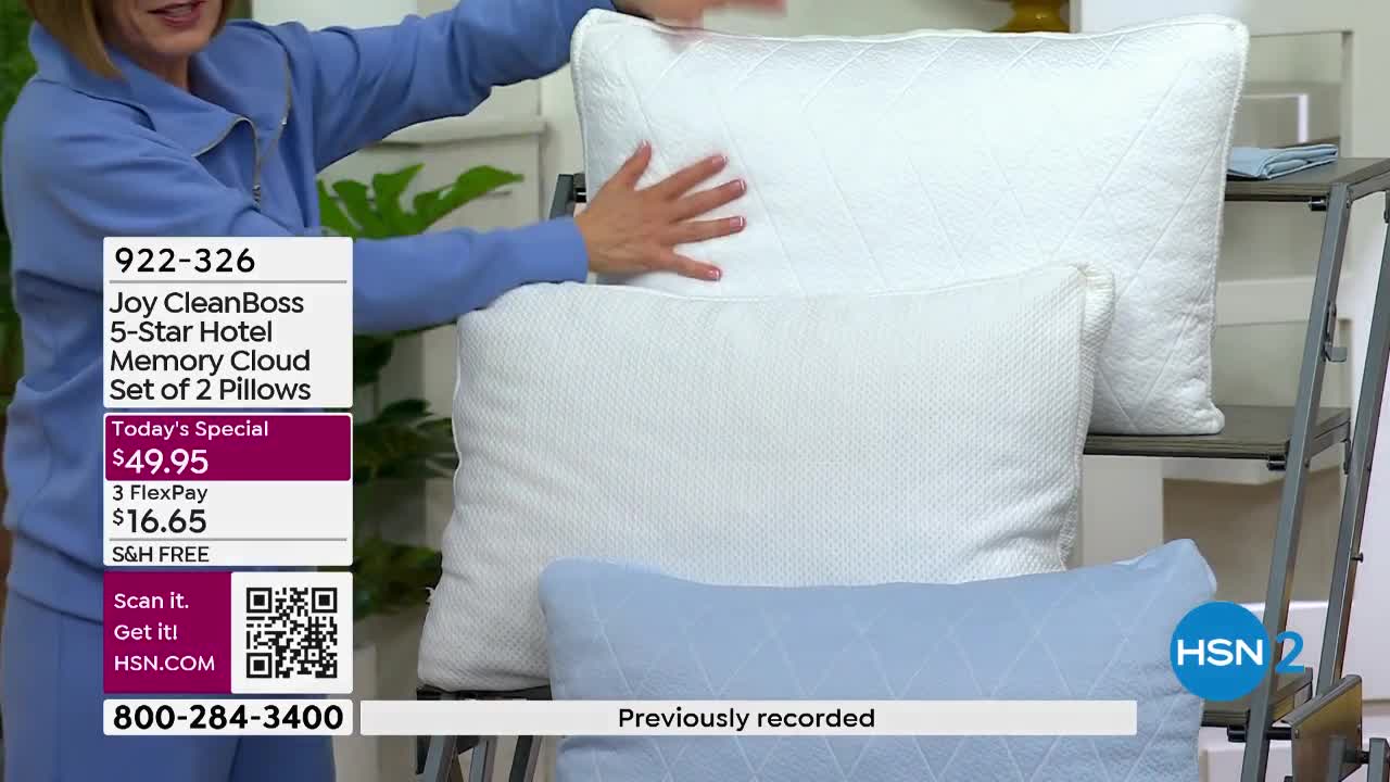 A woman's hand presses down on a large white pillow stacked on two others. The HSN logo flashes on screen next to a blue pillow.