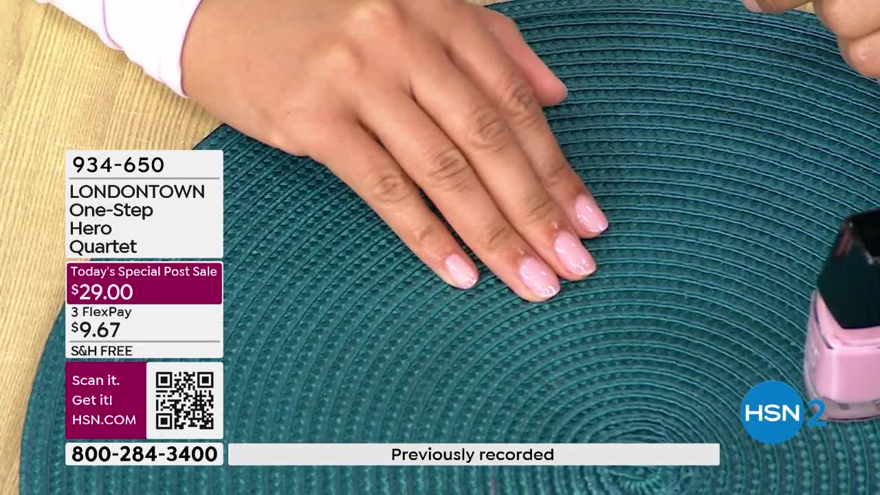 A hand with freshly painted pale pink nails rests on a teal placemat. A bottle of the same color polish sits to the right.