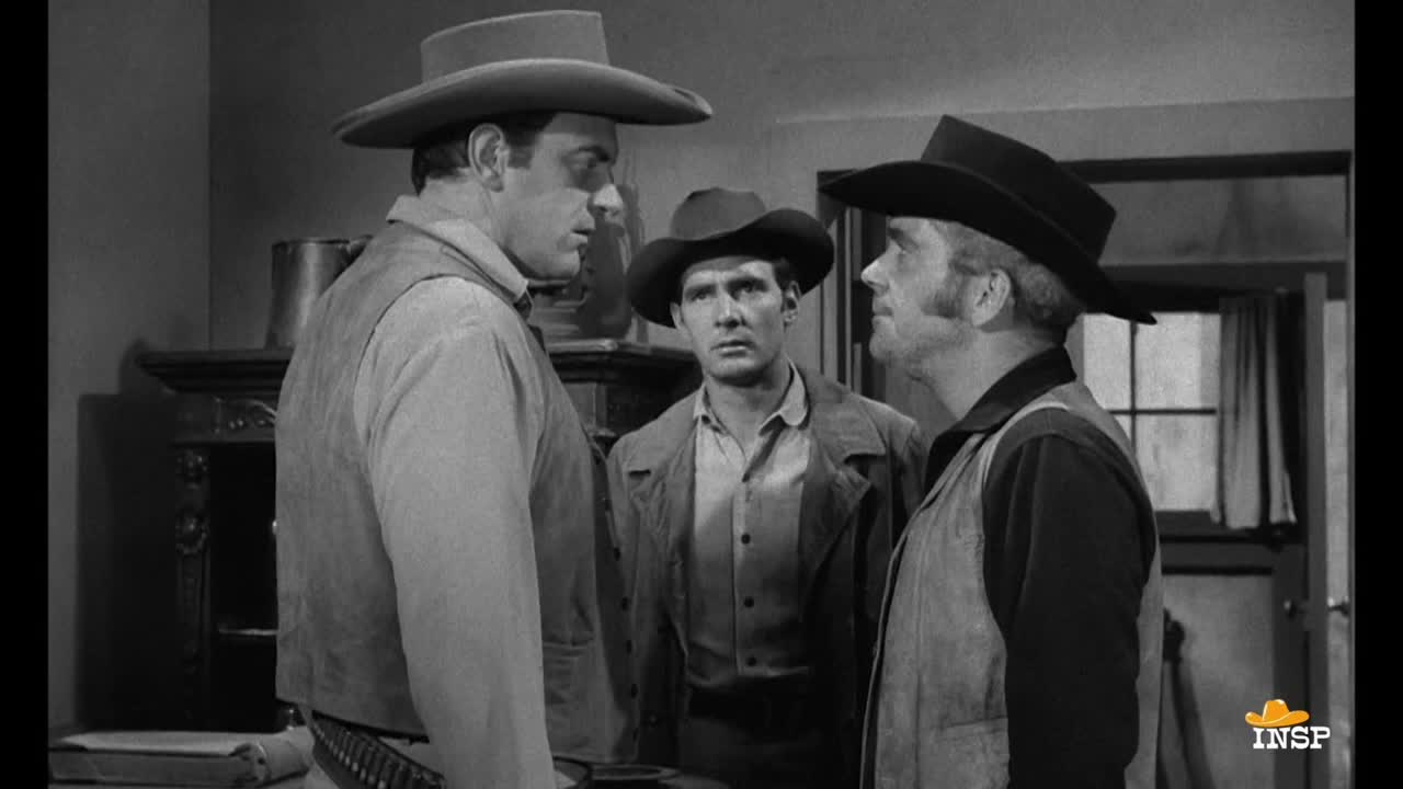 Three men in cowboy hats are facing each other, engaged in a serious conversation. The man in the center has a concerned expression, while the others look stern.
