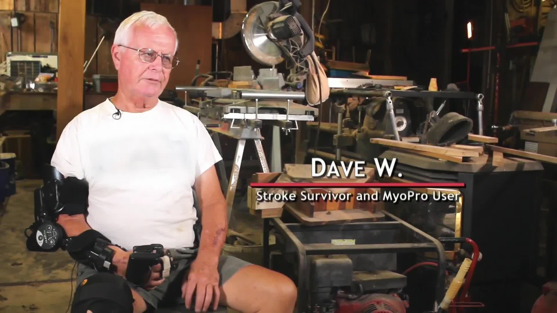 Dave W., a stroke survivor, sits in his workshop, wearing an arm brace. He's talking, and the camera is focused on him, with the tools and equipment of his trade visible in the background.
