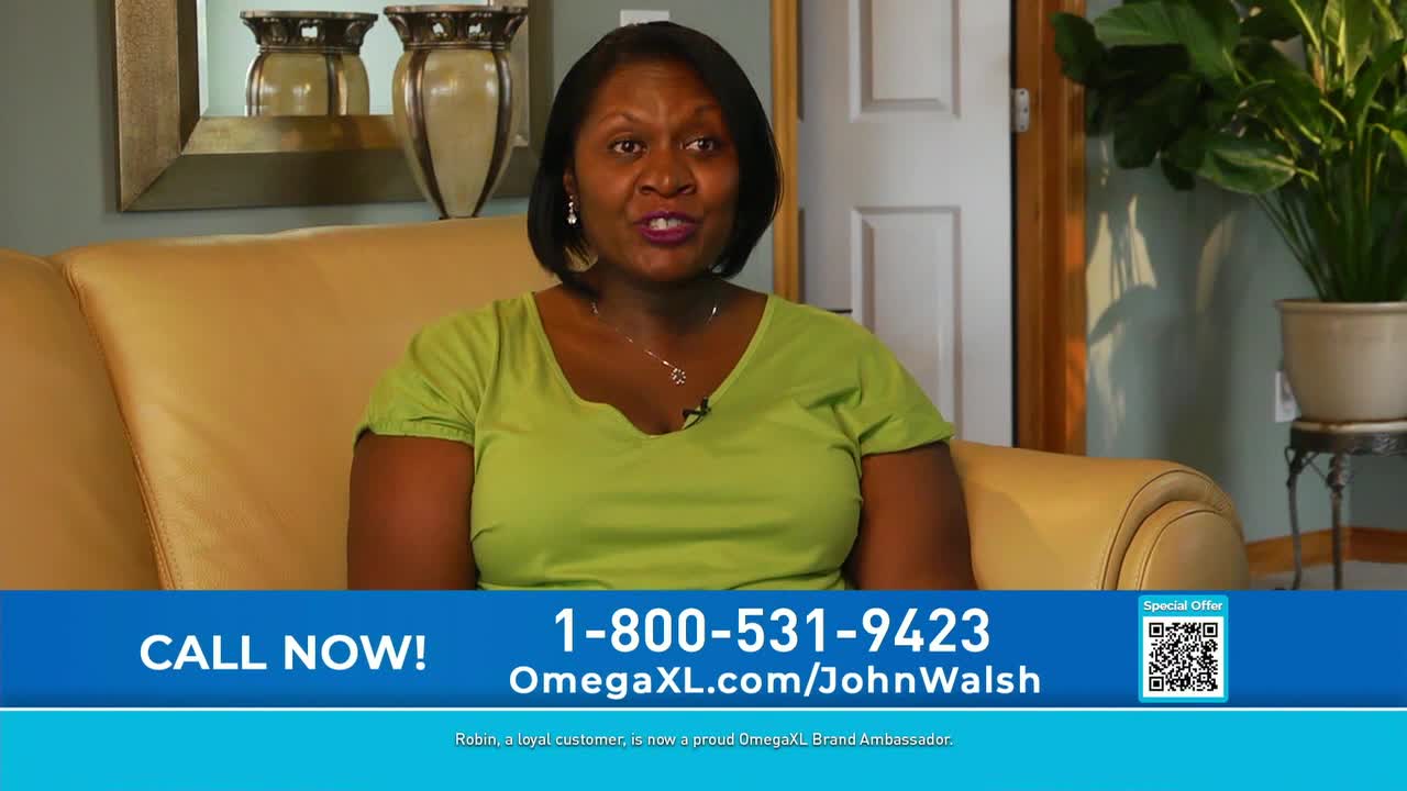 A woman in a green shirt sits on a beige couch, speaking directly to the camera. Below her, a blue banner displays a phone number and website address, advertising OmegaXL.

