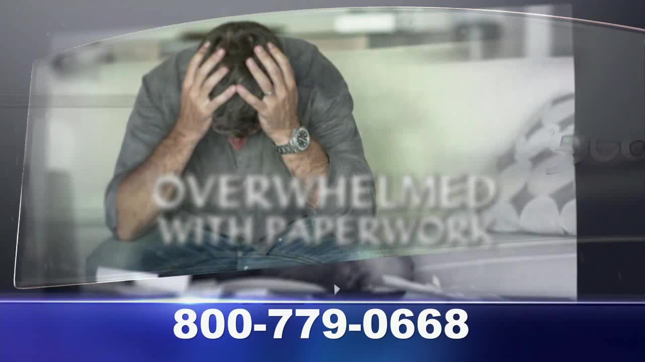 A man sits with his head in his hands, the words "OVERWHELMED WITH PAPERWORK" superimposed over him. Below, a phone number flashes on the screen, presumably for help.
