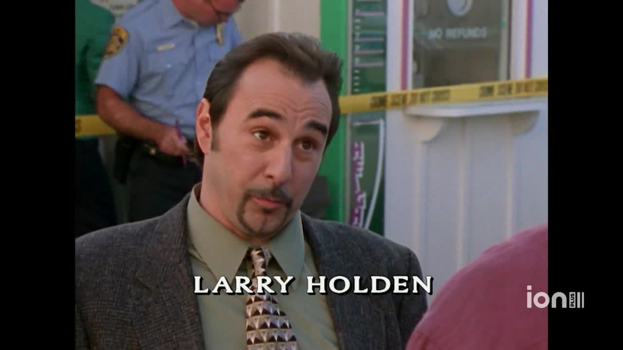 A man named Larry Holden, in a patterned tie and gray jacket, is looking directly at the camera. Behind him, a police officer stands near yellow caution tape, possibly at a crime scene, as the ION Plus logo appears in the corner.

