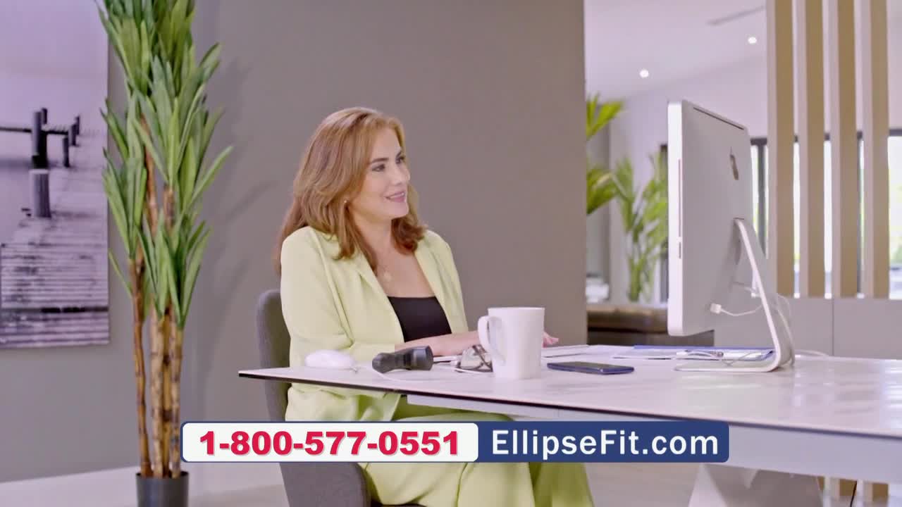 A woman in a light green blazer sits at a desk, smiling as she looks at her computer screen.  The EllipseFit.com phone number flashes across the bottom of the screen.
