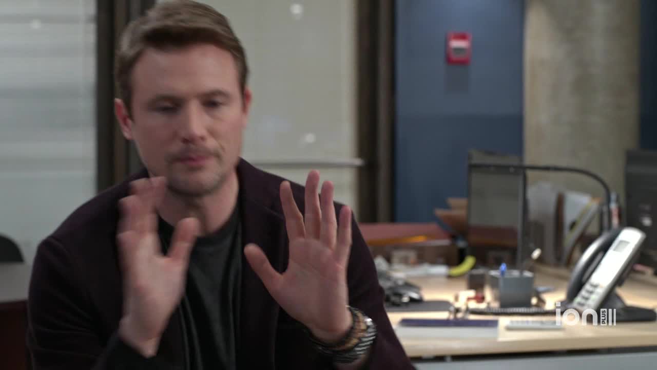 The man gestures with both hands, palms out, as if to stop something. He's in an office setting, and the ION Plus logo is visible in the corner.
