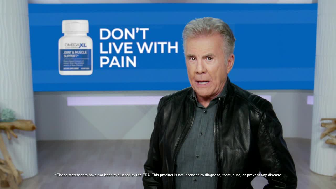 A man in a leather jacket stands in front of a blue backdrop, speaking directly to the camera. Behind him, a bottle of Omega XL is displayed with the words "Don't Live With Pain."
