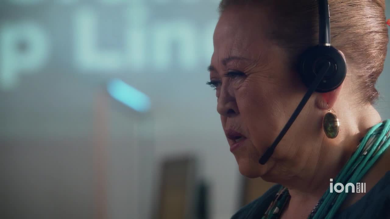 The woman in the headset is speaking, her mouth slightly open. Behind her, a blurry sign reads "Help Line," and the ION Plus logo is visible in the corner.
