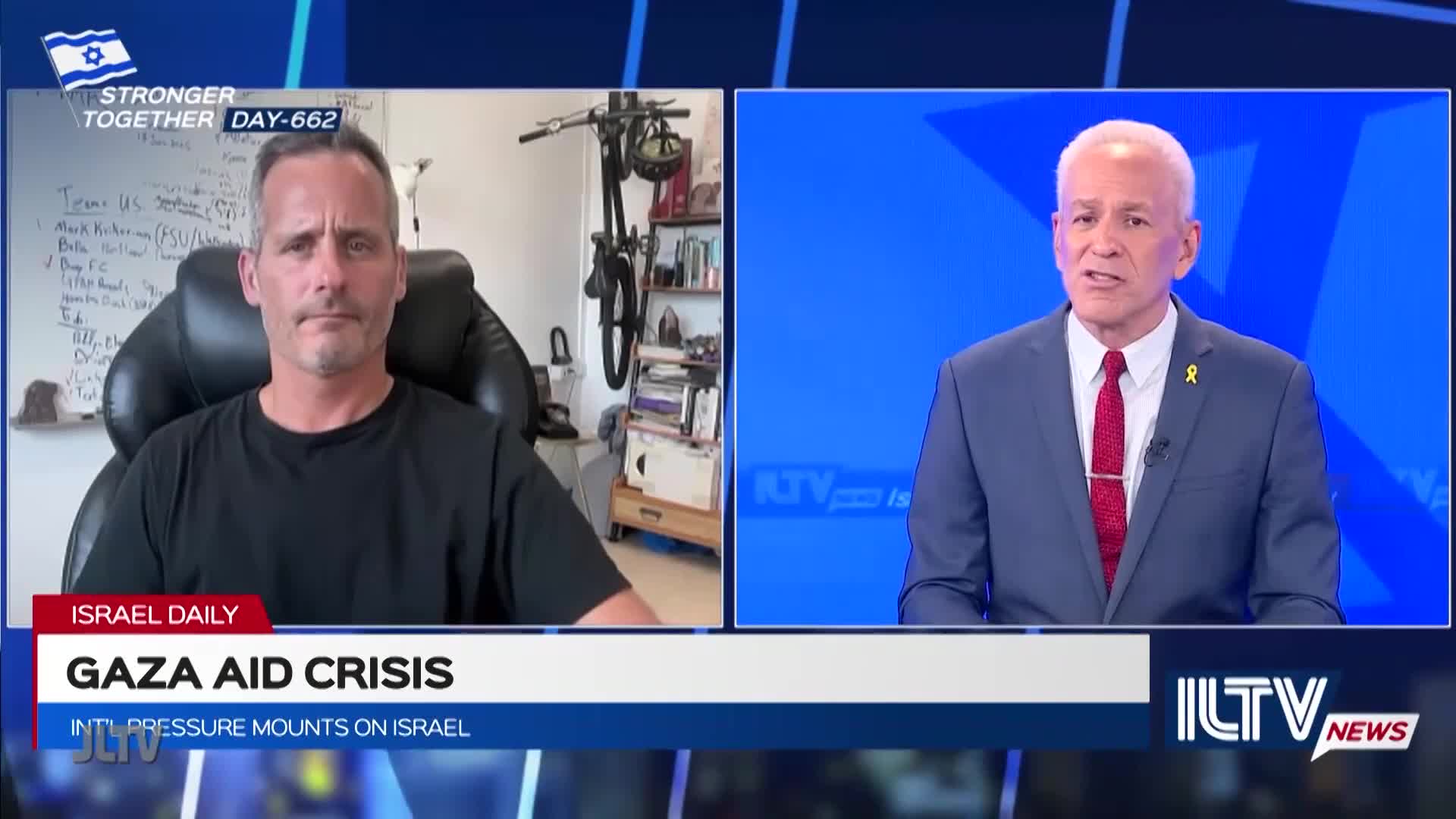 On Jewish Life Television, a man in a black t-shirt is being interviewed; his expression is serious. Across the screen, a news anchor in a suit speaks, with a yellow ribbon pinned to his lapel.

