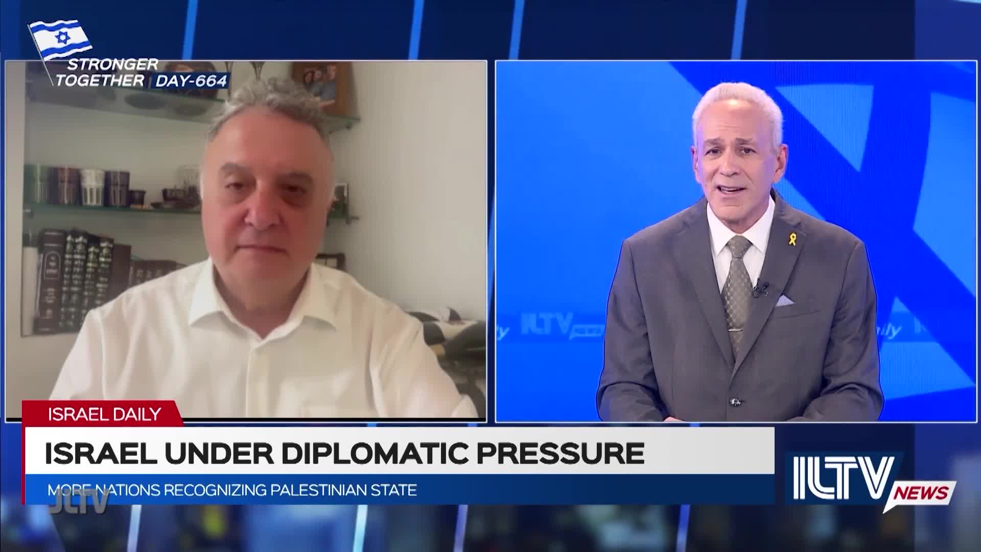 On Jewish Life Television, a man in a white shirt is on a screen, while a man in a suit speaks from a studio set. The broadcast focuses on Israel and the diplomatic pressure it faces.
