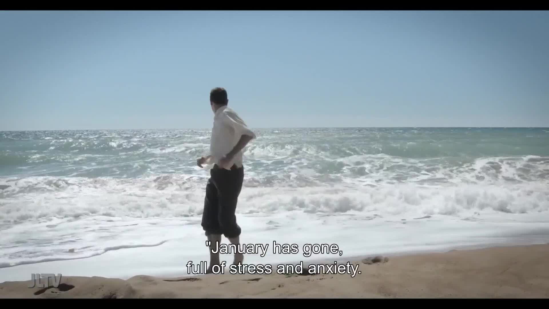 A man in a white shirt and dark pants runs along the shoreline, the waves crashing behind him. The scene, likely from Jewish Life Television, seems to capture a moment of reflection.
