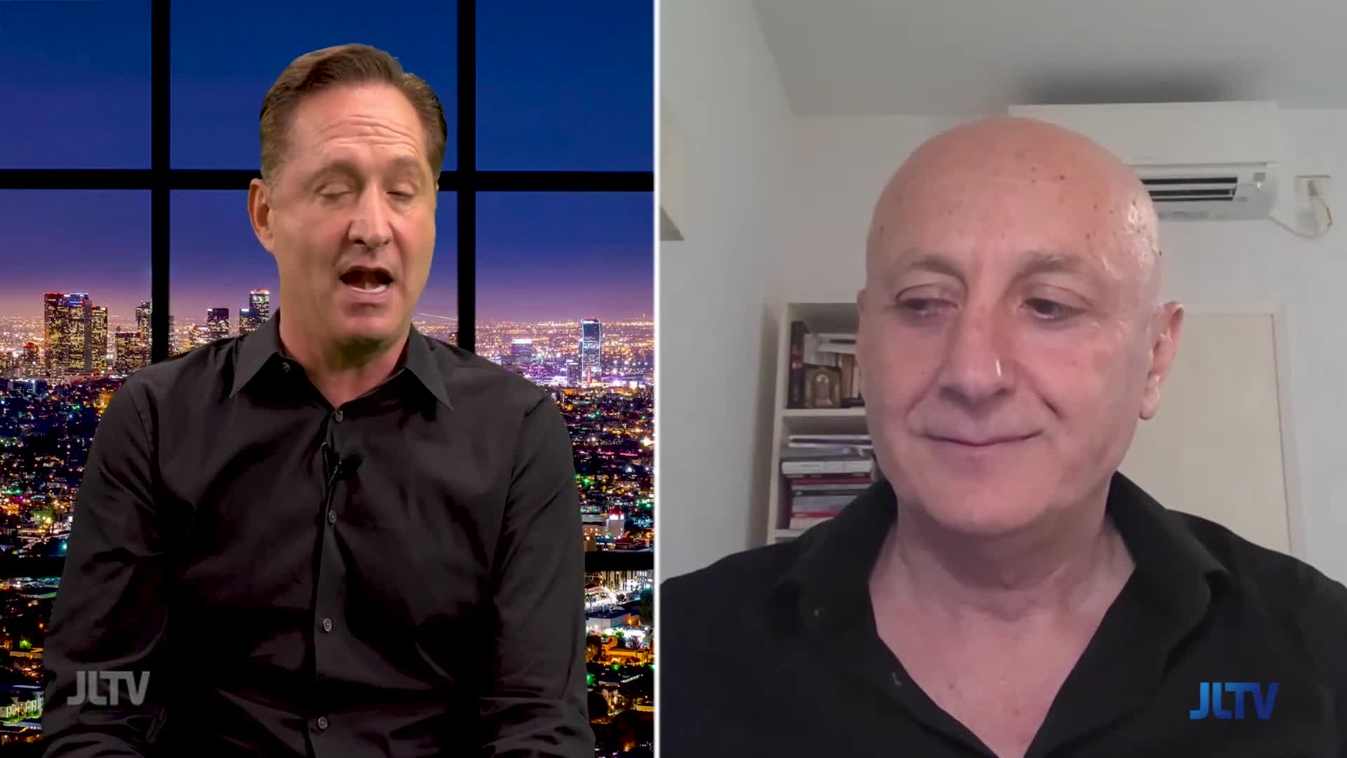 The man on the left, in a black shirt, is speaking, his mouth open. Across the screen, another man listens, a slight smile on his face, appearing on Jewish Life Television.
